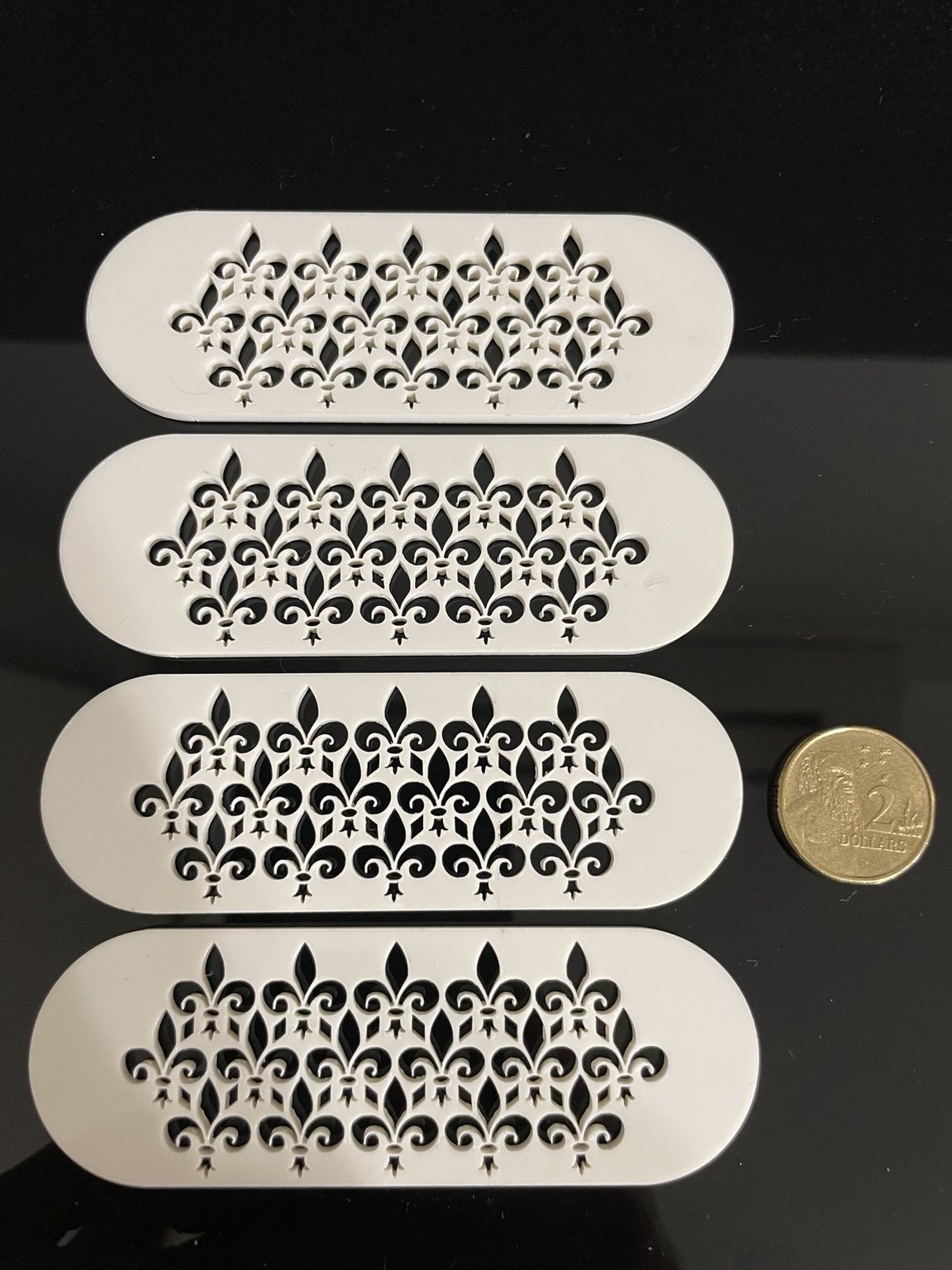 Small detailed white acrylic cut pieces beside an Australian two dollar coin for scale